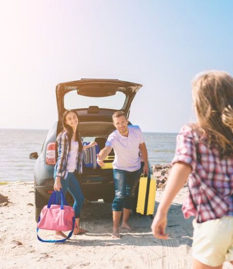 Young couple standing near the opened car boot with suitcases and bags. Dad, mom and daughter are traveling by the sea or the ocean or the river. Summer ride by automobile